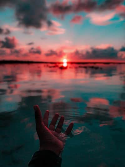 5 Ways To Get The Best From Your Virtual Team virtual assistant Blog. The image is of a hand reach out over the water to a beautiful red sunset