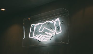 The Return To ‘Normal’; What Does This Mean For Remote Workers And Businesses? virtual assistant blog. The image is of a neon shine showing a handshake